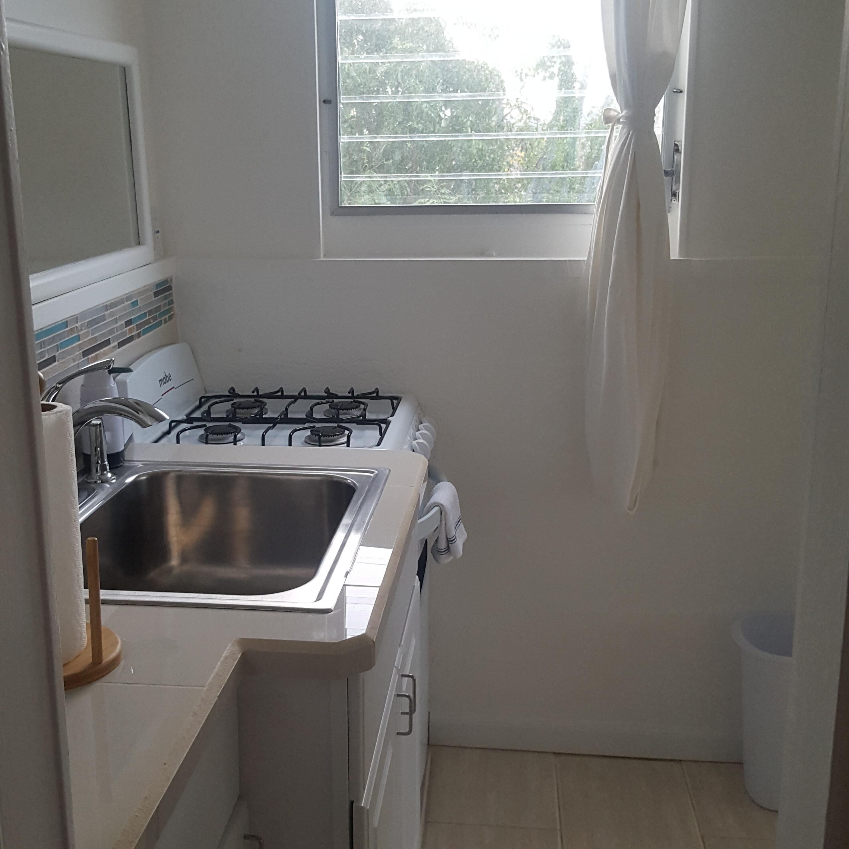 A compact kitchen with a gas stove, stainless steel sink, and a small window.