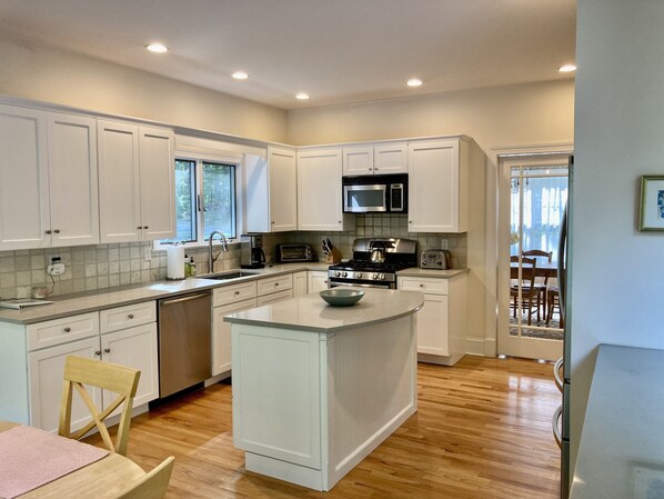A modern kitchen with white cabinets, a central island, stainless steel appliances, and a wooden dining table with chairs.