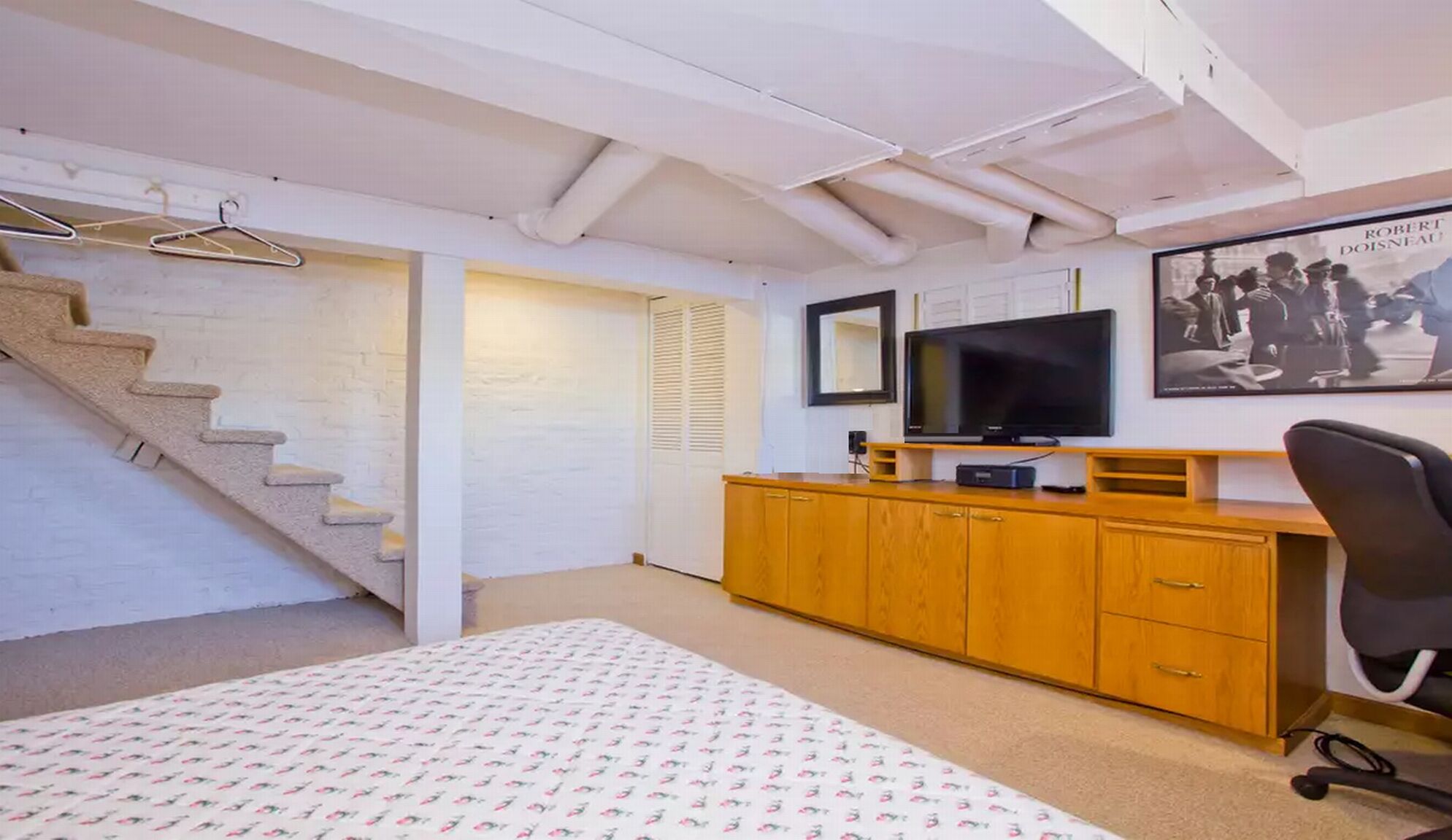 A bedroom with a bed, wooden dresser, TV, and a staircase.