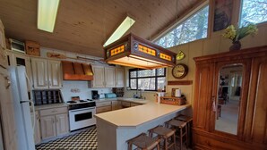 A kitchen with wooden cabinets, a stove, a sink, and a bar area with stools.