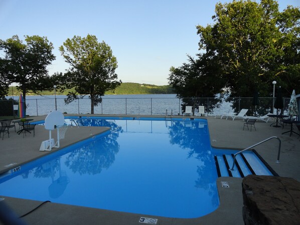 Relax by the pool surrounded by comfortable seating and shaded by trees, with lounge chairs and umbrellas nearby.
