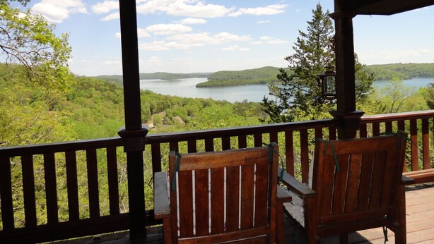 A wooden deck with two chairs overlooking a lake surrounded by greenery.