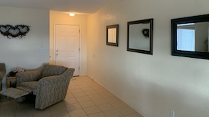 A hallway with a door, a patterned armchair, and three framed mirrors on the wall.