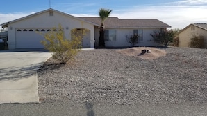 A single-story house with a garage, a gravel driveway, and a small tree in the front yard.
