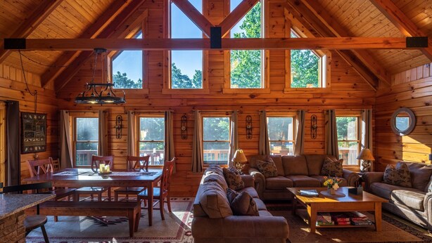 L’intérieur d’une cabane en rondins comprend un coin repas, un salon avec des canapés et de grandes fenêtres.
