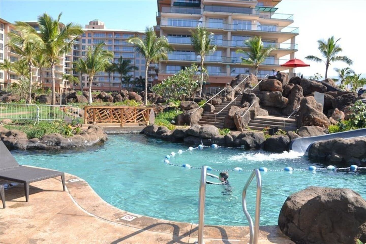 Een zwembadgedeelte met een waterglijbaan, palmbomen en een meerlaags hotel op de achtergrond.