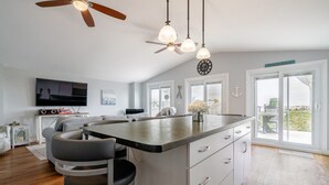 A modern kitchen with a central island, bar stools, a ceiling fan, pendant lights, and large windows with a view. - Another Sunset by the Bay: Waterfront - 2-Bedroom (Leamington)