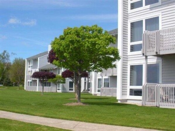 A multi-story residential building with a central tree, a visible balcony, and a well-maintained lawn.