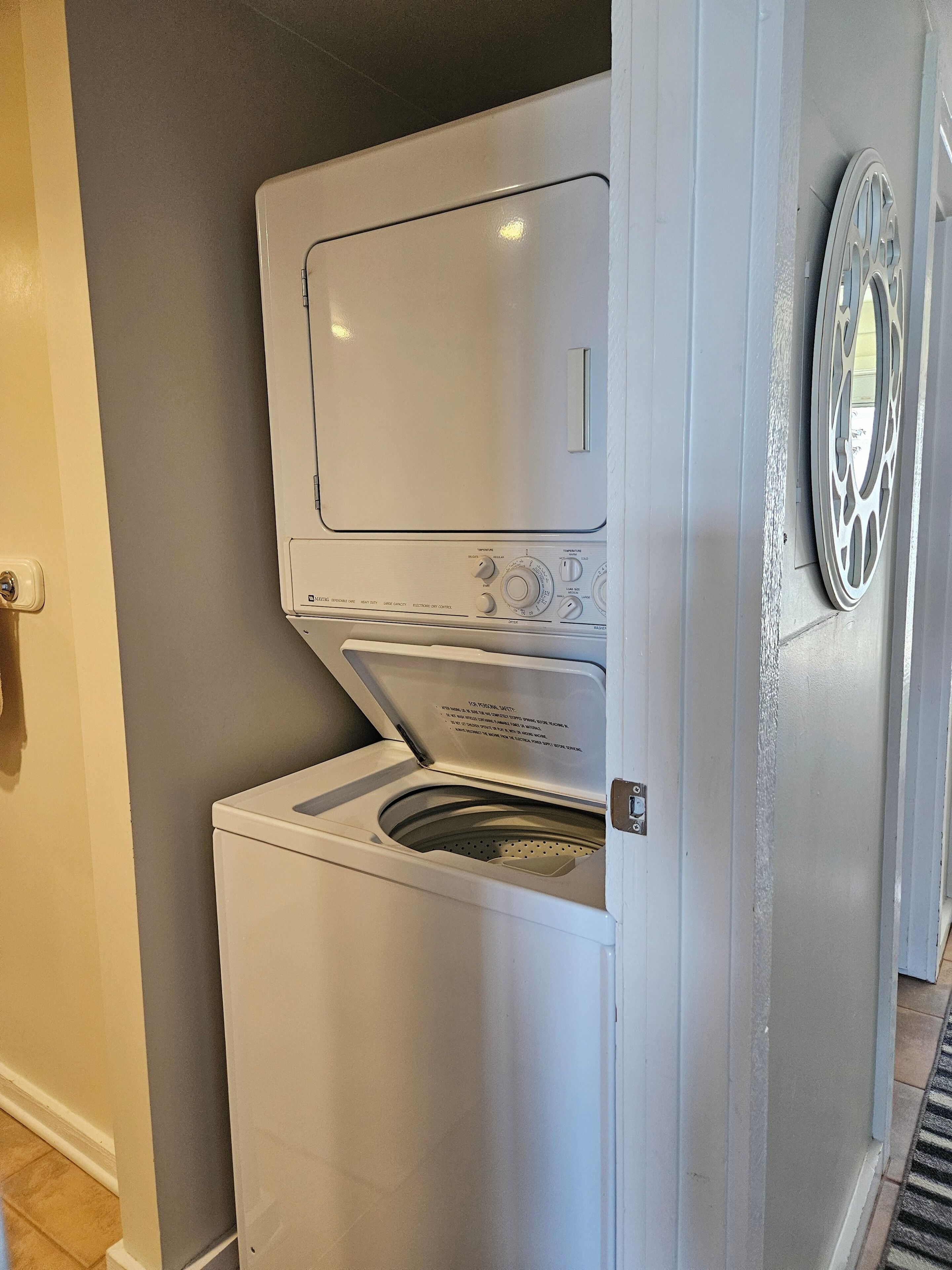 Une machine à laver à chargement frontal se trouve dans une buanderie, avec un mur gris et une porte sur le côté gauche.