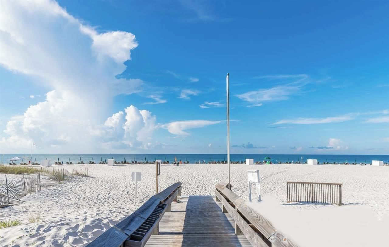 A wooden boardwalk leading to a sandy beach with a clear sky.
