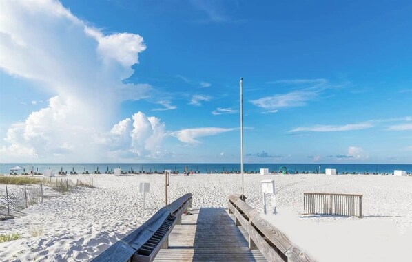 A wooden boardwalk leading to a sandy beach with a clear sky.