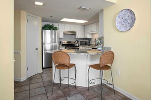 A modern kitchen with white cabinets, stainless steel appliances, and a central island with two wicker bar stools.