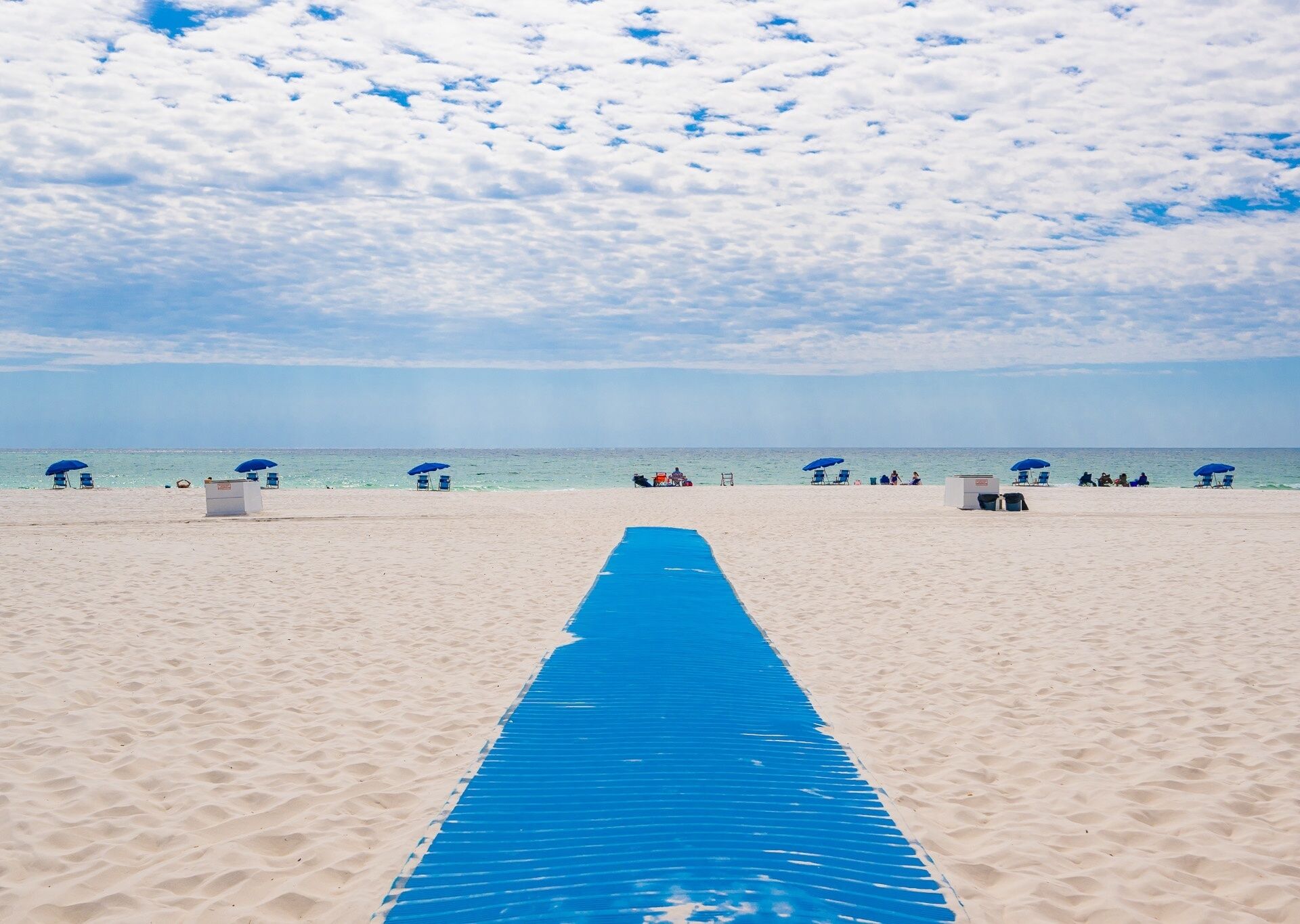 Une plage avec un chemin bleu menant à l’eau, des parasols bleus et des chaises de plage.