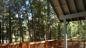 A wooden deck with a railing overlooking a forested area. - SPECTACULAR COZY CABIN NESTLED IN THE PINES BIG FRONT DECK FENCED FOR DOGS (PINETOP)