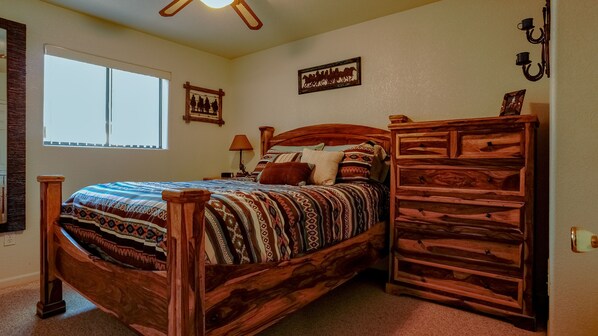 Een slaapkamer met een houten bed, nachtkastje, dressoir en een raam met jaloezieën.