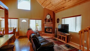 A spacious living room with a fireplace, a television, and a dining area with a table and chairs. - SPECTACULAR COZY CABIN NESTLED IN THE PINES BIG FRONT DECK FENCED FOR DOGS (PINETOP)