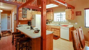 A cabin-style kitchen with wooden cabinets, a central island with stools, a coffee maker, and a dishwasher. - SPECTACULAR COZY CABIN NESTLED IN THE PINES BIG FRONT DECK FENCED FOR DOGS (PINETOP)