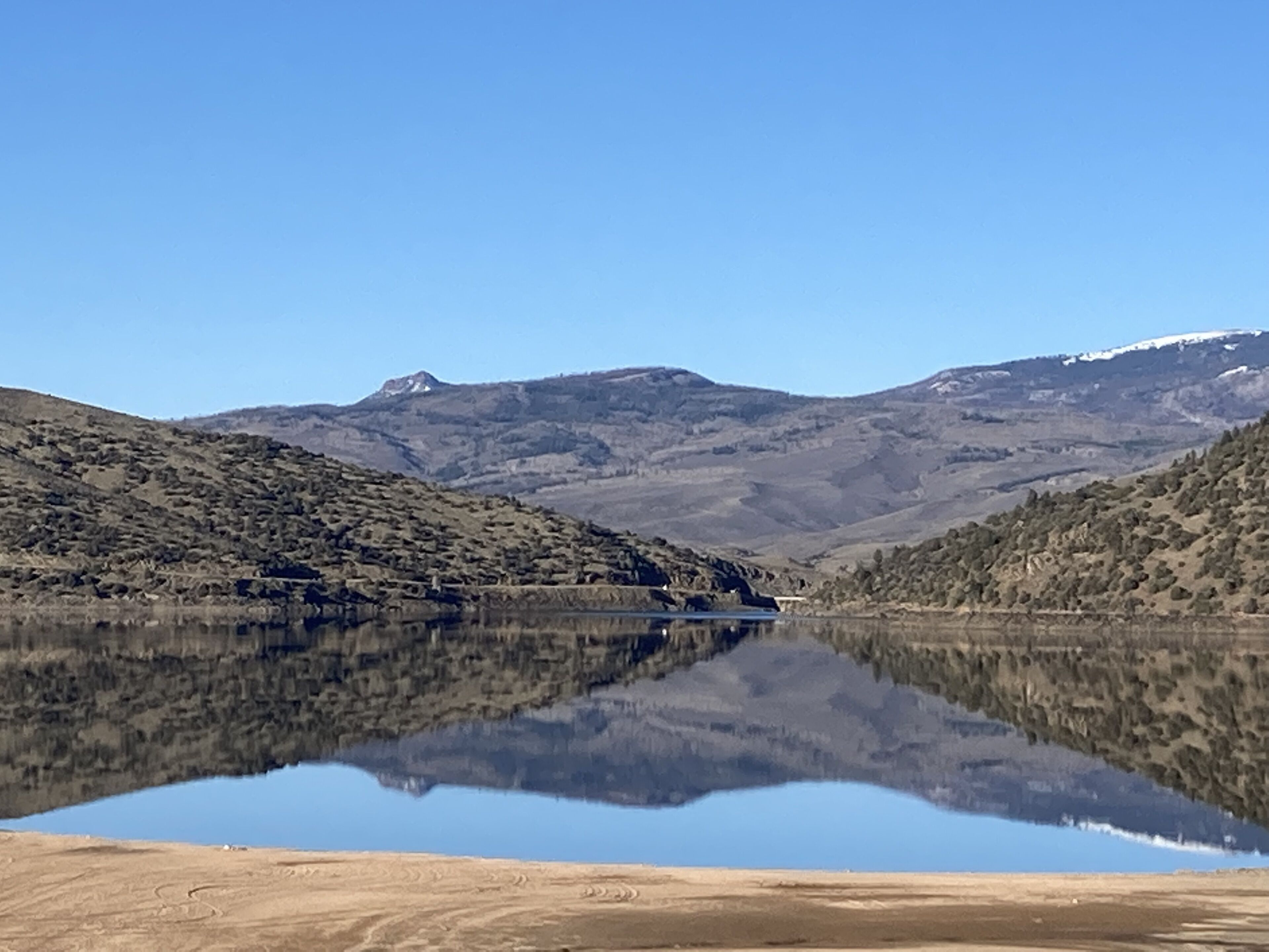 A calm lake with a clear reflection, surrounded by hills and a mountain in the distance.