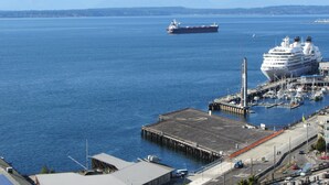 Un puerto con un gran crucero amarrado en un muelle, rodeado de montañas y un cielo despejado.