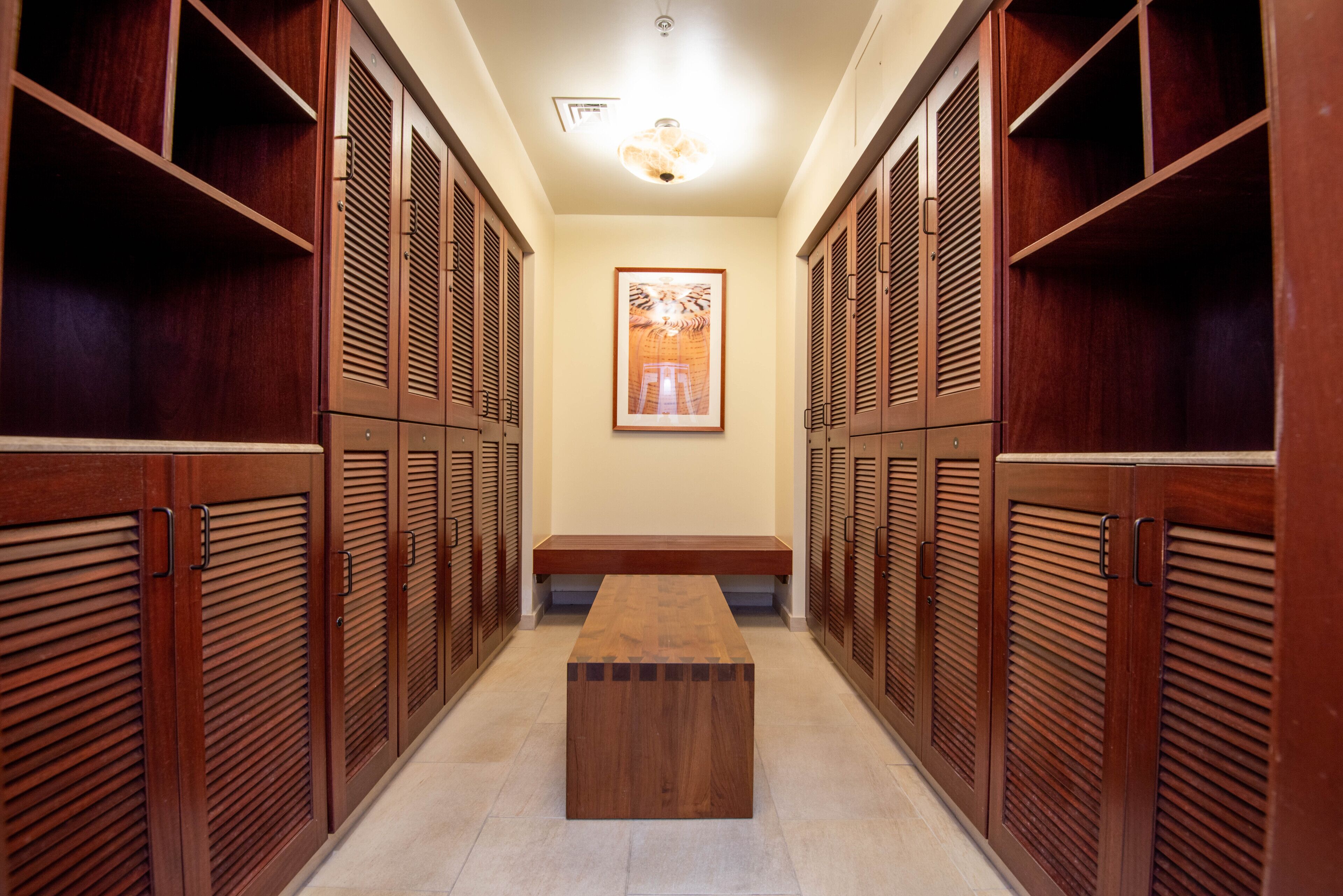 A hallway with wooden lockers, a bench, and a framed picture on the wall.