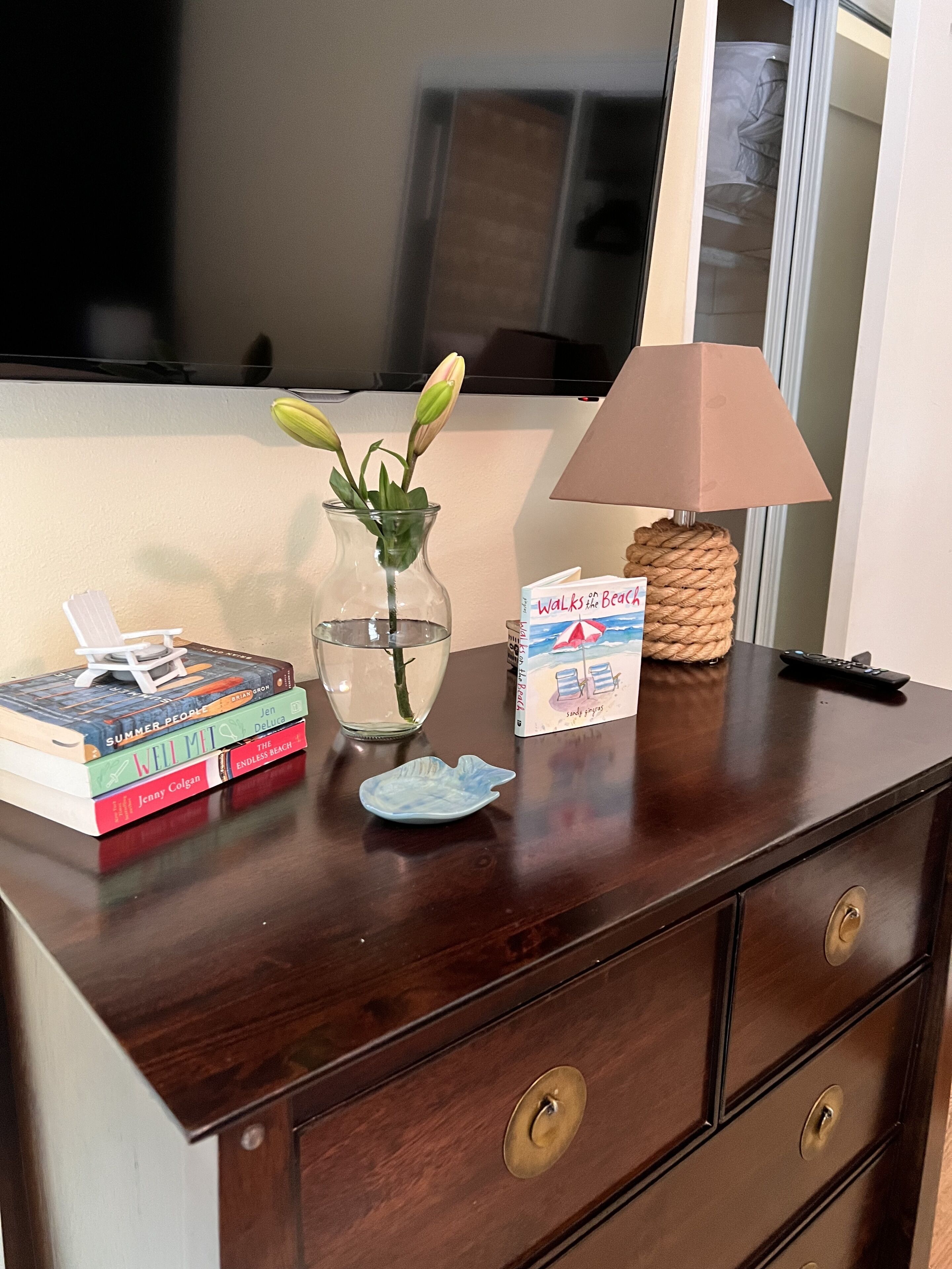 Une commode en bois avec un miroir, un vase de fleurs, une lampe et des livres.