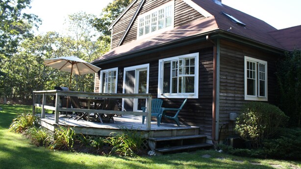 A wooden house with a porch, a covered patio, and a chimney.