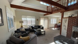 A spacious living room with a high ceiling, a fireplace, and a dining area with a table and chairs.