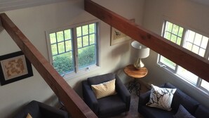 A spacious living room with a high ceiling, large windows, and a wooden beam structure.