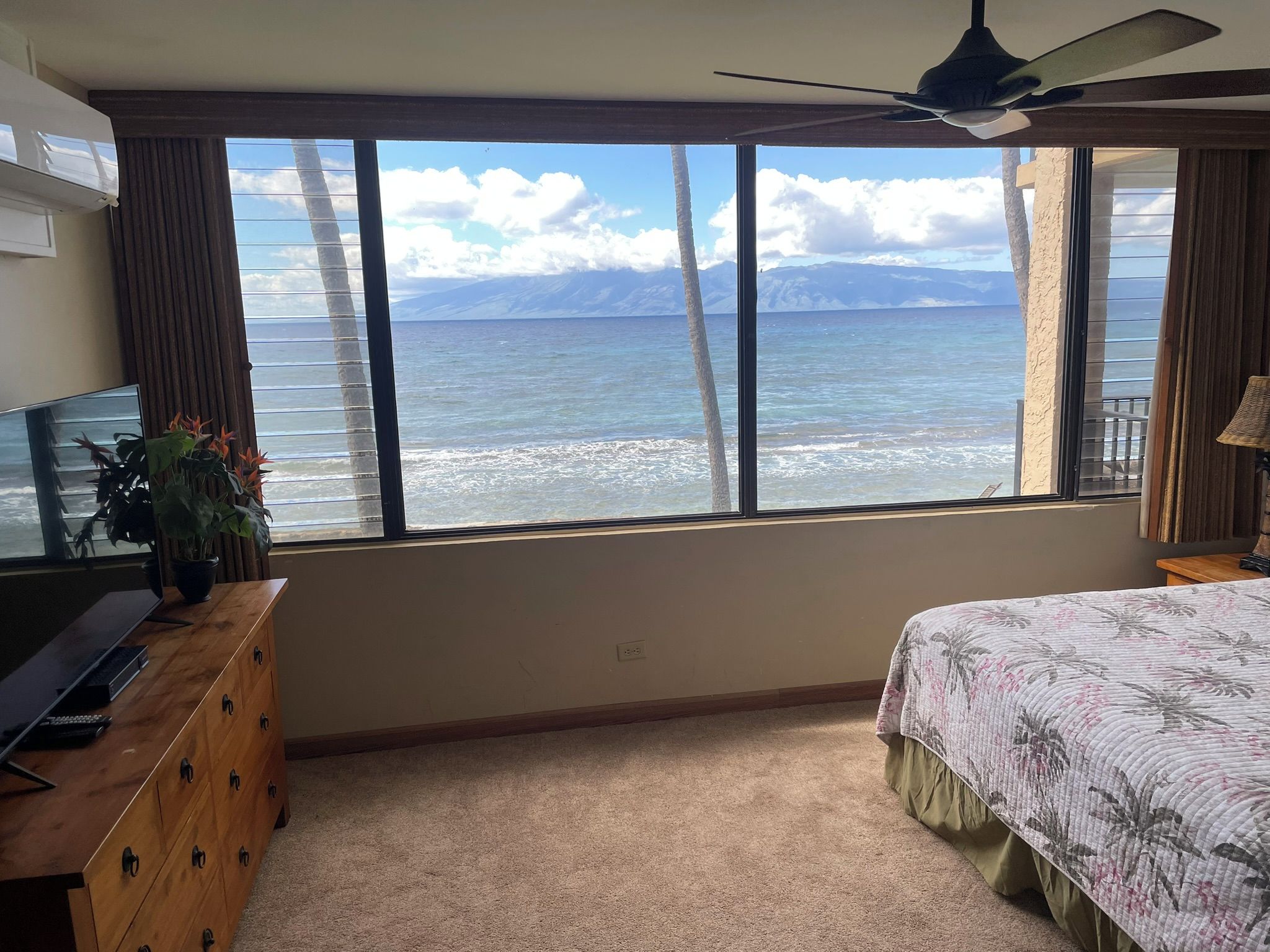 A bedroom with a large window, a bed, a desk, and a ceiling fan.