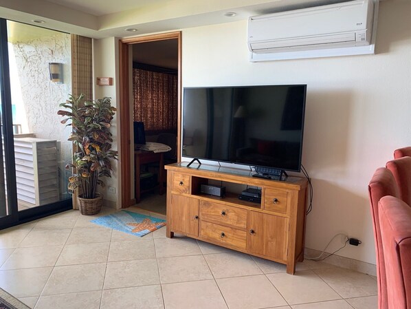 Un salón con televisor sobre un mueble de madera, una planta en maceta y un tapete con motivos de estrellas en el suelo.