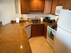 Une cuisine dotée de plans de travail en granit, d’armoires en bois, d’un lave-vaisselle, d’une cuisinière et d’un four à micro-ondes.