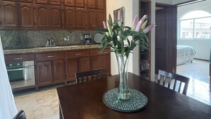 Een moderne keuken met houten kastjes, een granieten aanrecht en een eettafel met stoelen. Op tafel staat een vaas met bloemen.
