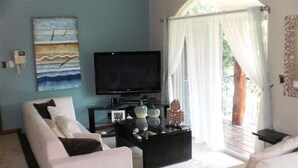 Een woonkamer met een witte bank, een zwarte salontafel en een flatscreen televisie.