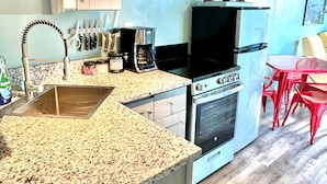 Cocina compacta con lavabo, cafetera, estufa y comedor con sillas rojas.
