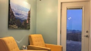 Una habitación con dos sillones amarillos, un cuadro de un paisaje montañoso, una lámpara en el techo y una puerta que da a un paisaje.