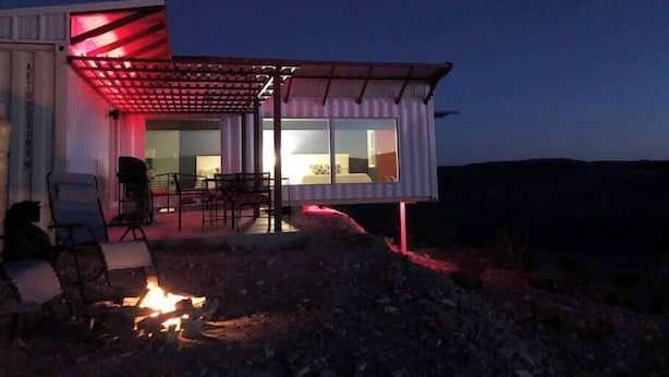 Una casa moderna con un porche cubierto, un brasero y vista al interior.