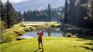 En golfbane med en sø, omgivet af træer og bjerge i baggrunden.