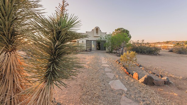 A desert landscape with a building featuring a distinctive arched entrance and a gravel pathway leading to it.