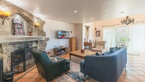 A cozy living room with a stone fireplace, comfortable seating, a television, and a large window with curtains.