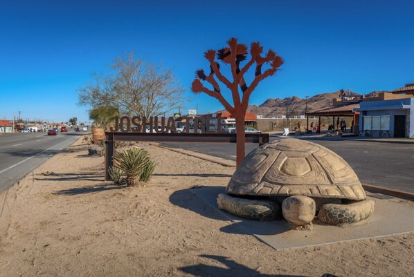 A desert landscape with a large tortoise sculpture, a sign reading 'JOSHUA TREE,' and a clear blue sky. - Hot Tub Stargazing with Amazing Desert Views (Joshua Tree)