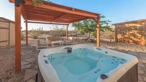 A hot tub under a wooden pergola with a patio area, including chairs and a table.