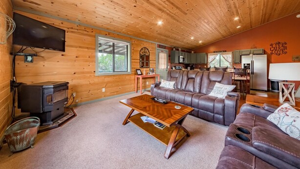 A cozy cabin interior with a wooden ceiling, a leather sofa, a coffee table, a TV, and a kitchen area.