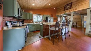 A cozy kitchen with wooden cabinets, a dining area with metal chairs, and a visible clock on the wall.