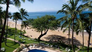 A beach with palm trees, a pool, and a view of the ocean. - Spectacular Beachfront  at Hale Pau Hana. You never leave the beach when you stay with us. (Kihei)