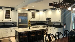 Una cocina moderna con armarios blancos, una isla central con taburetes de bar, un refrigerador de acero inoxidable y una estufa a gas.