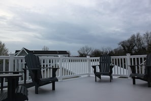 Relax in style on this covered deck, featuring Adirondack chairs and a small table.