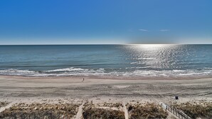 Una playa con cielo despejado, mar tranquilo y una persona caminando.