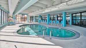 Una piscina interior con indicador de profundidad de 6 pies, rodeada de sillas azules y una zona cubierta con techo blanco.