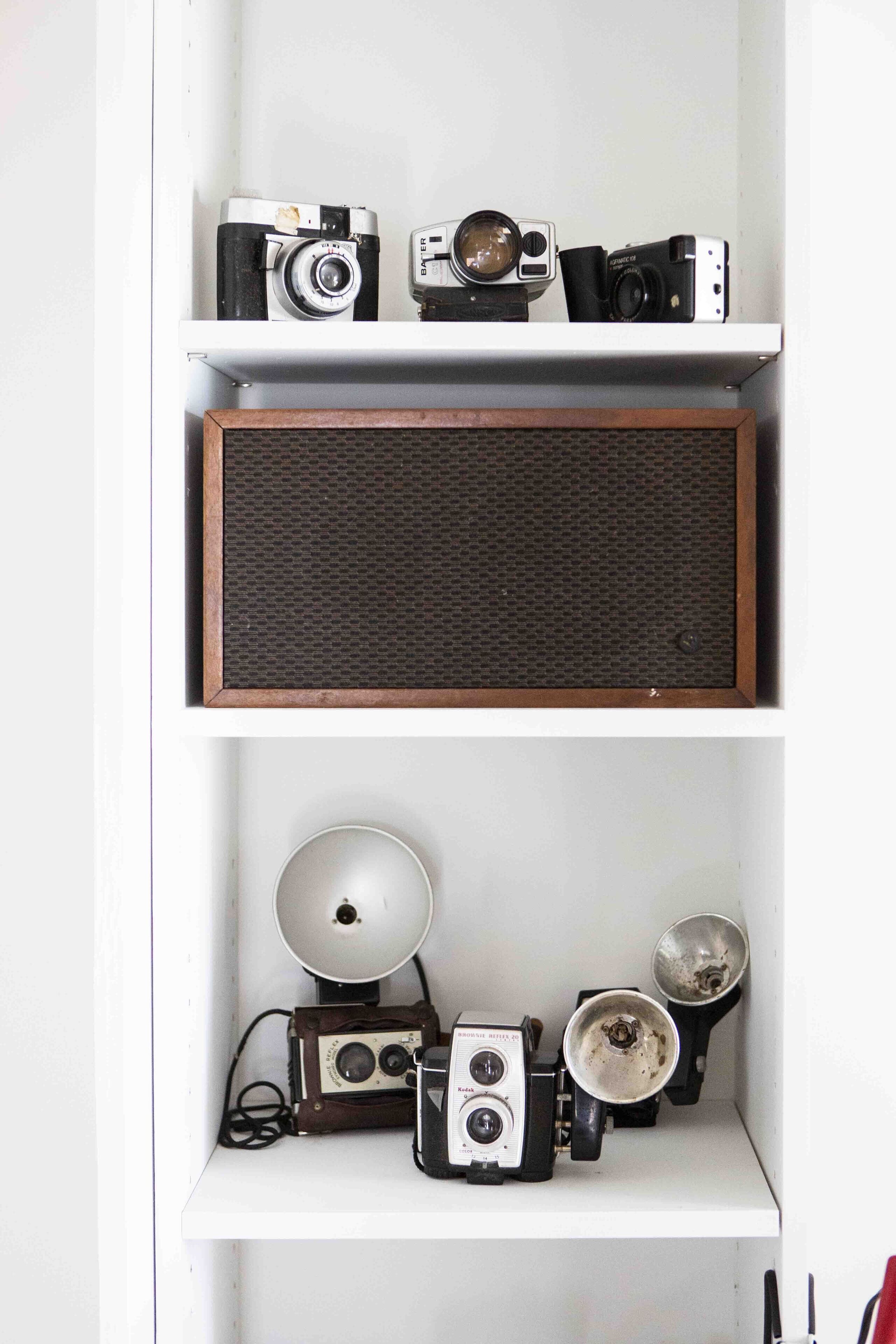 Een witte plank met vintage camera's en een speaker.