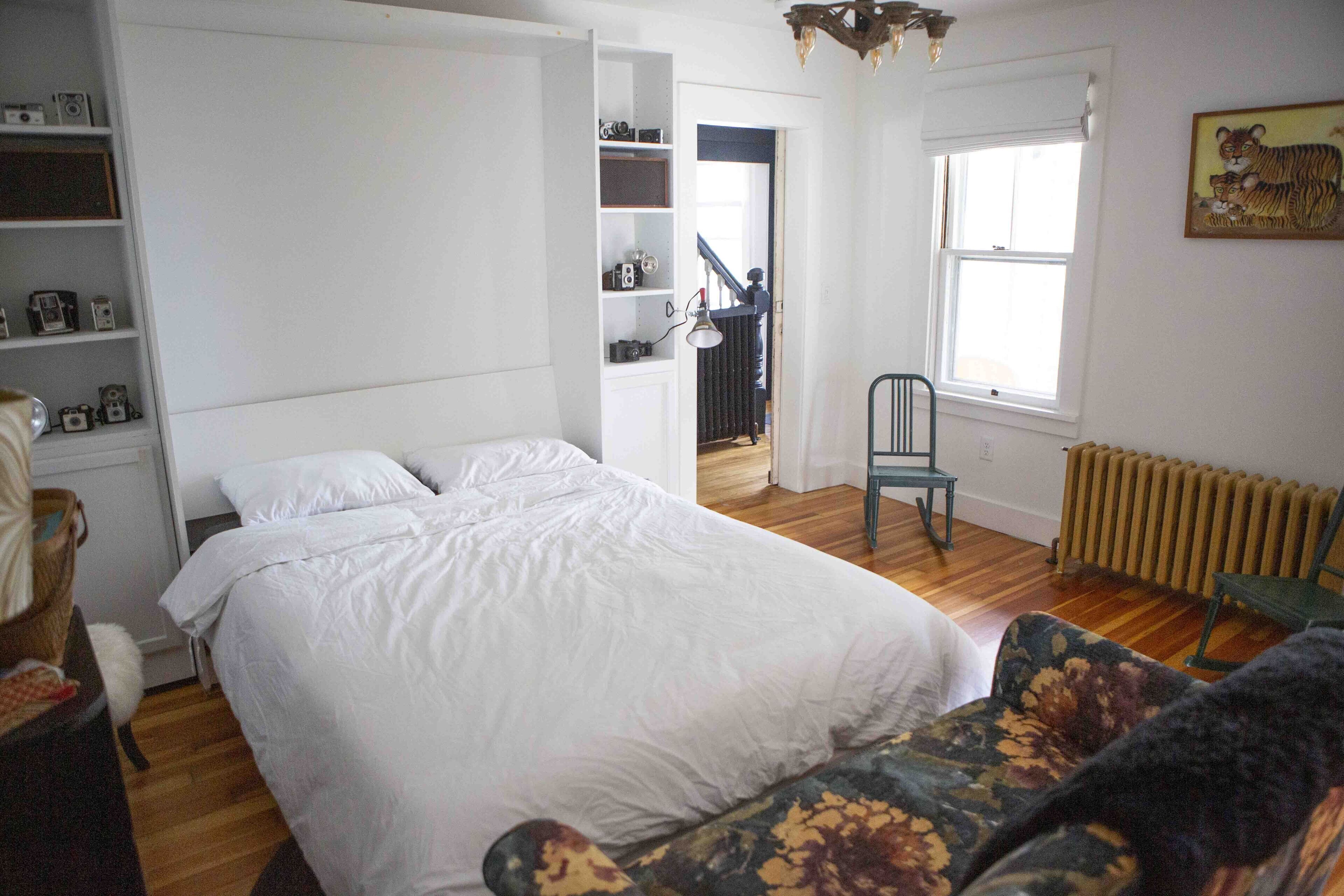 A bedroom with a large bed, a chair, a radiator, and a bookshelf.